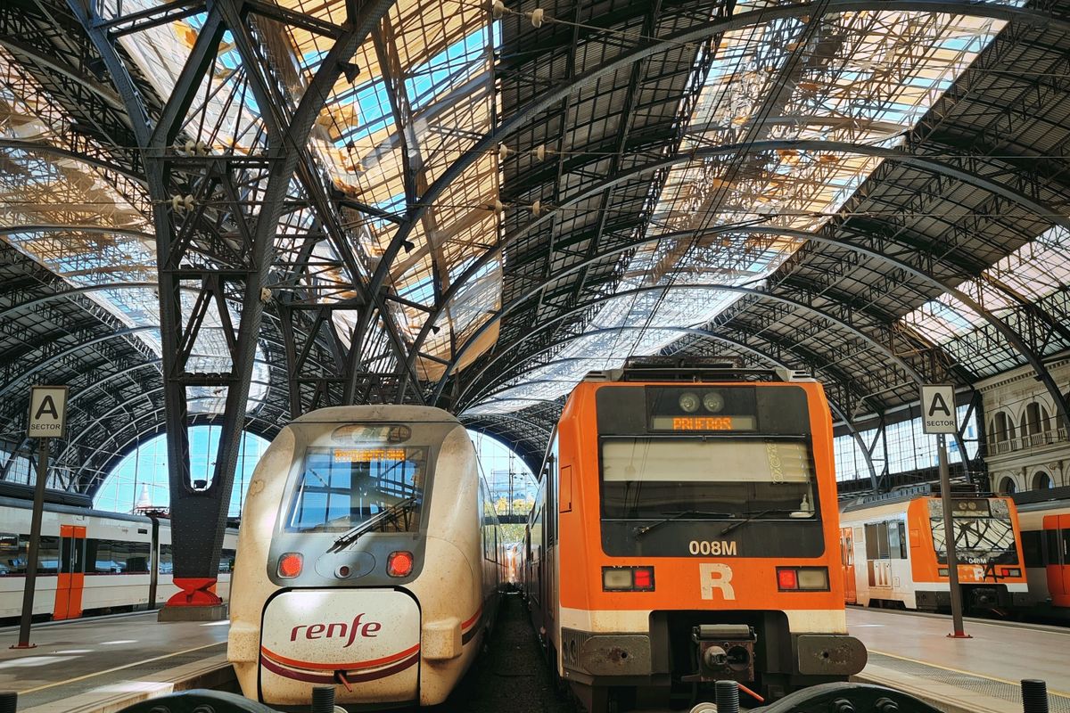 Two Renfe regional trains under the arched iron roof of a Barcelona terminus