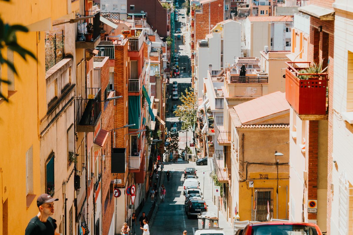 A narrow Barcelona street in Gràcia sloping downhill between low coloured buildings with balconies
